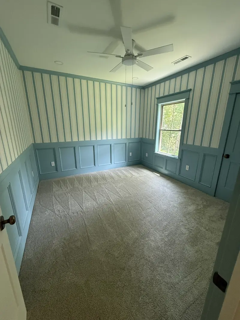 Finished bedroom with blue wainscot panels and striped wallpaper