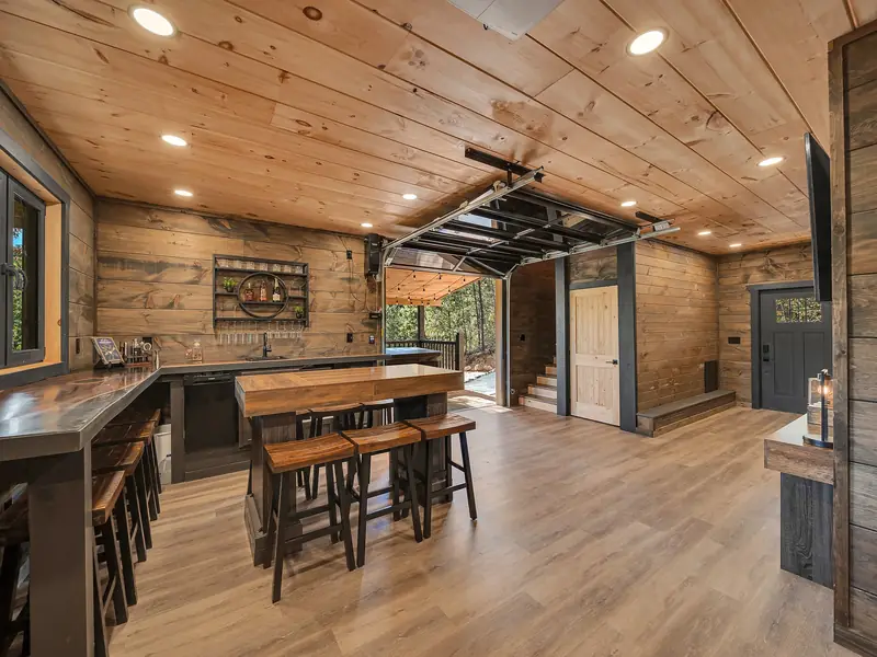 Cabin Project: wood-paneled bar area with stools and a garage-style door open to the outdoors