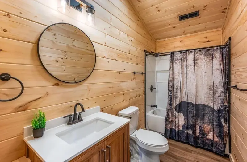 Cabin Project: wood-paneled bathroom with a round mirror and shower