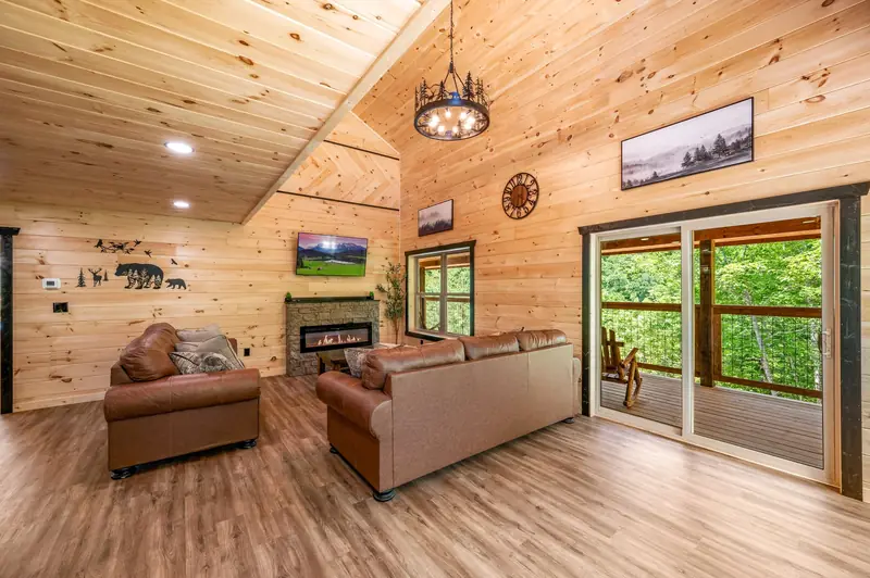 Cabin Project: living room with wood-paneled walls, fireplace and sliding door to a balcony