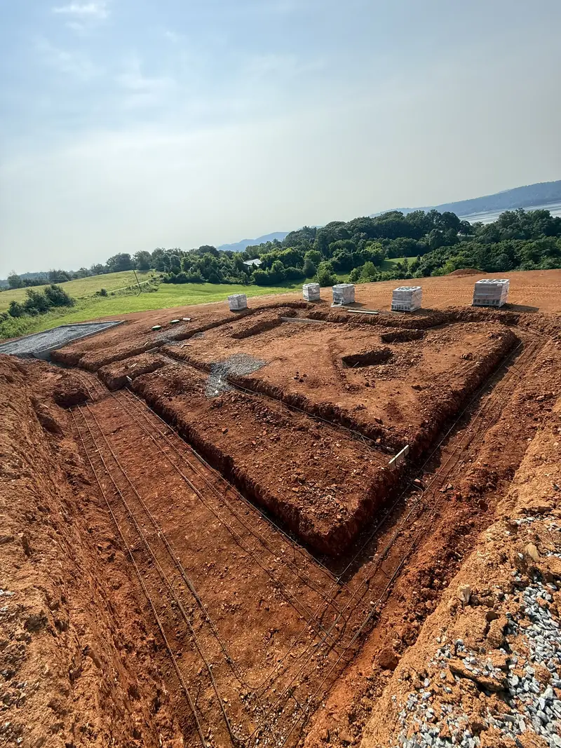 Excavated footings with rebar and block pallets on a new home site with a lake and mountain view
