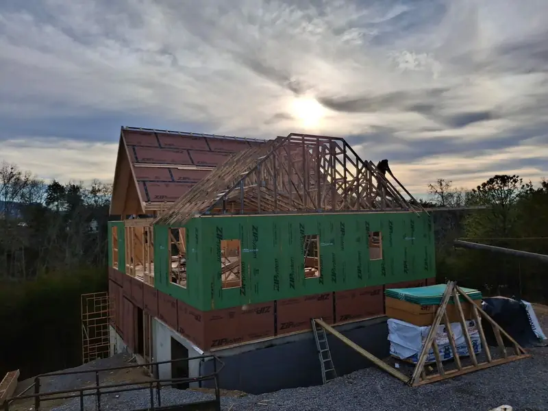 Two-story house framing with green-sheathed walls and roof trusses set over a block foundation, East Tennessee