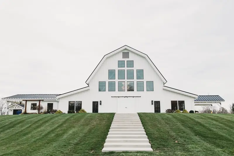 Large white gambrel-roof barn with tall windows and a long walkway across a mowed lawn