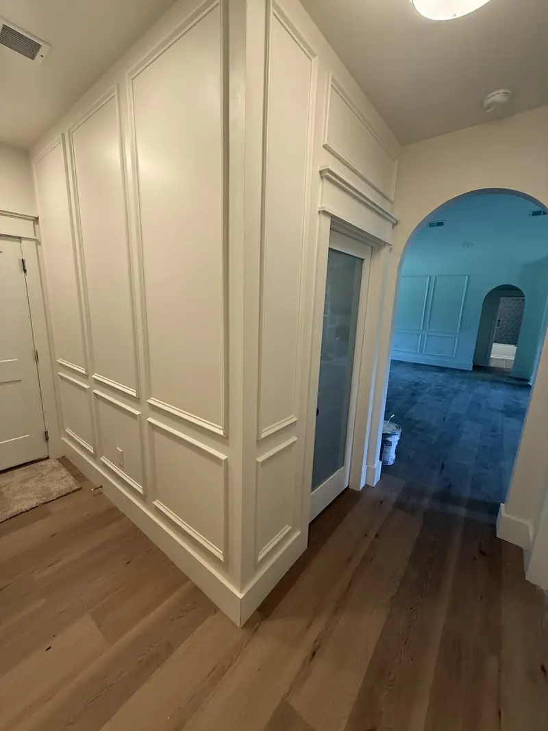 Finished hallway with full-height wall paneling and trim, an arched doorway and LVP flooring