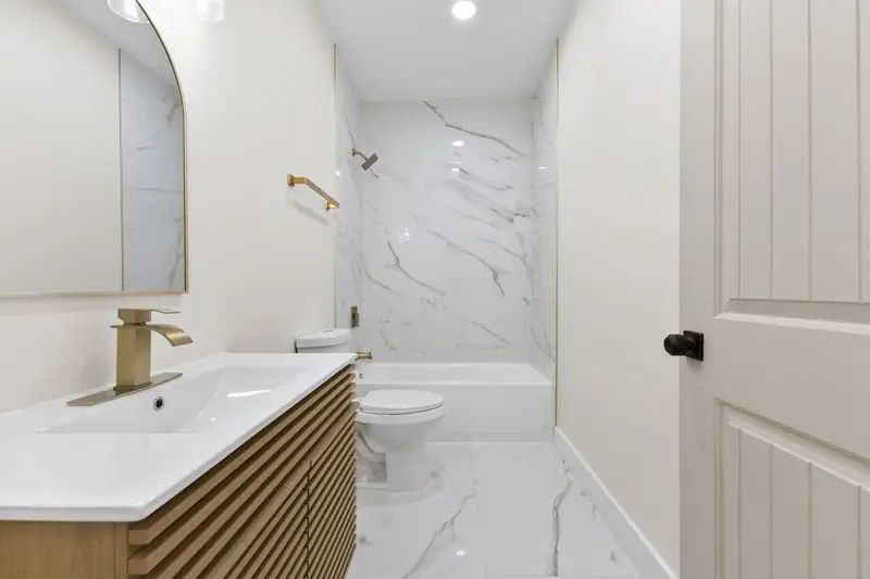 Hoppers Bluff spec home, Rutledge, TN: bathroom with marble walls and floors, wood vanity and gold faucet