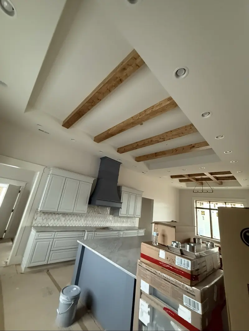 Kitchen at trim-out stage with white cabinets, a slate range hood and wood ceiling beams