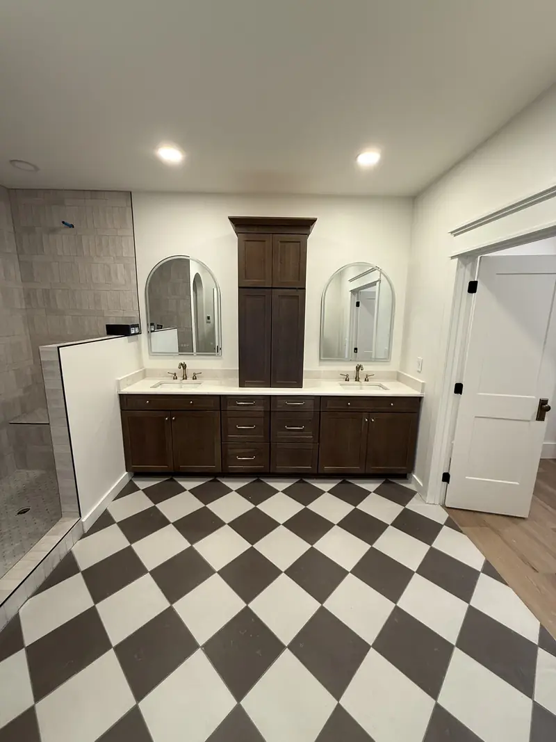 Finished master bath with checkerboard tile floor, dark double vanity, arched mirrors and tile shower