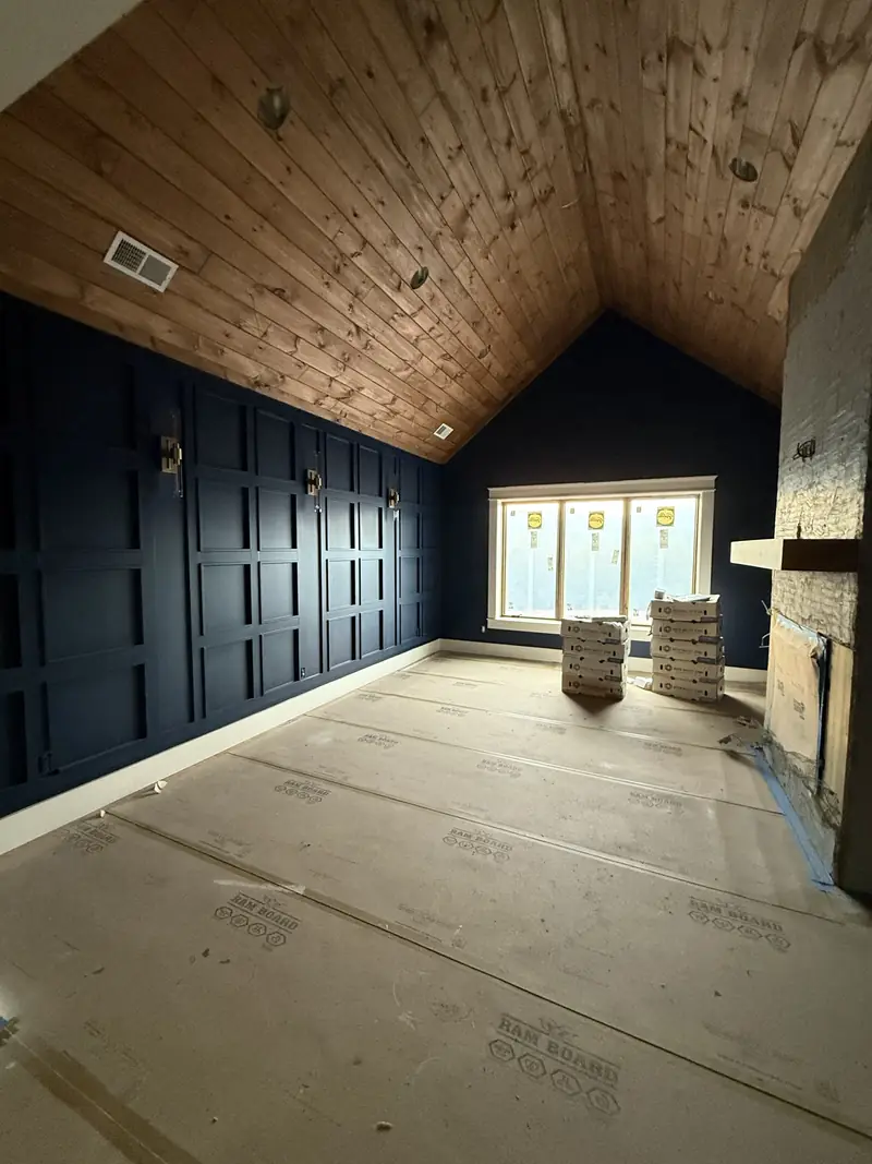 Room with navy board-and-batten wall paneling and a vaulted wood tongue-and-groove ceiling during the finish stage