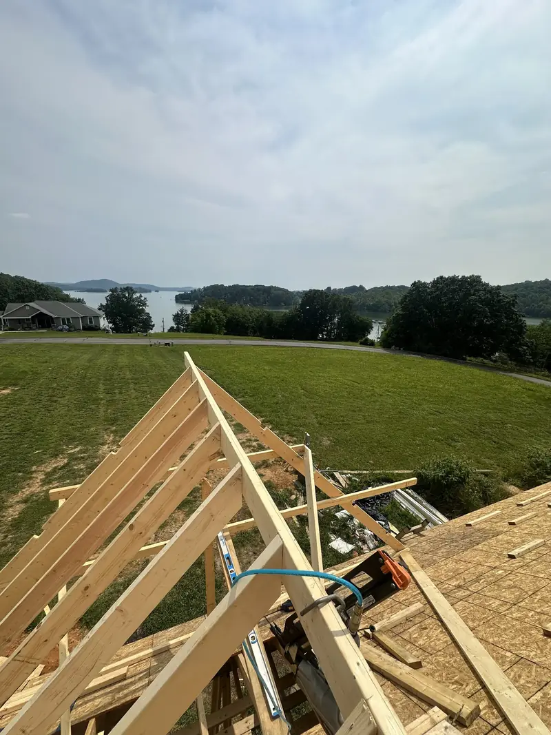 Roof trusses going up on a new build, with a green field and a lake in the distance