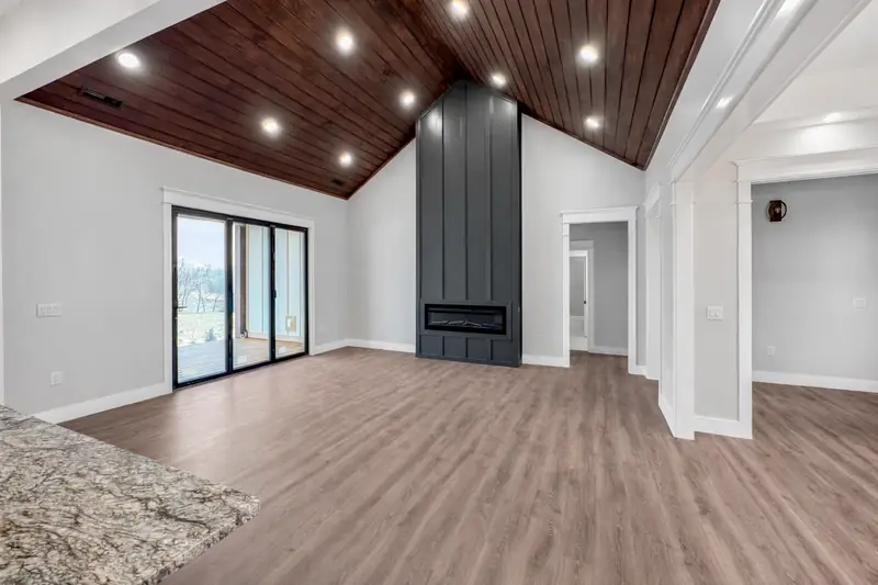 Shiloh Project: living room with hardwood floors, dark wood vaulted ceiling, black fireplace and sliding glass doors